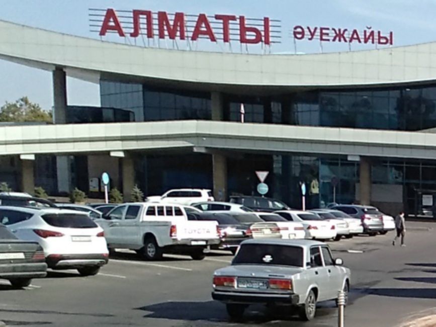 Terminal lotniska w Ałmaty w Kazachstanie, z charakterystycznym napisem cyrylicą i retro samochodami na parkingu.